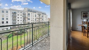 Ein Balkon mit Blick auf ein mehrstöckiges Gebäude, eine Essecke mit Tisch und Stühlen sowie ein Poster an der Wand.