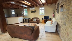Uma sala de estar aconchegante com um sofá marrom, uma poltrona branca, uma mesa de centro de madeira, uma televisão e uma parede de pedra.