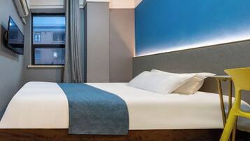 Quarto de hotel com cama, cadeira, televisão e janela com cortinas.