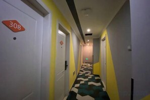 Et hotels korridor med døre mærket med værelsesnumre, et skakternet gulv og et loft med indbyggede spots.