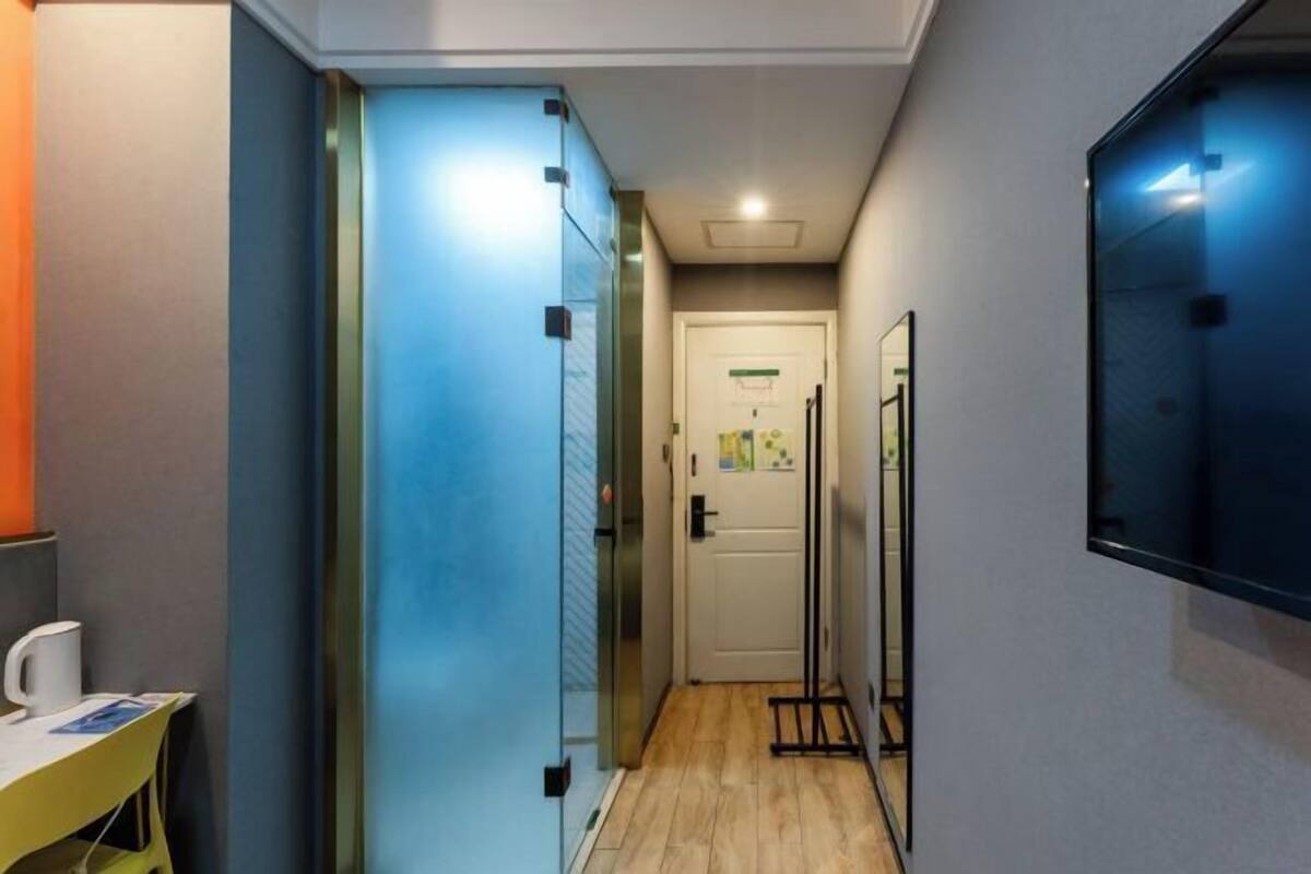 A narrow hallway with a wooden floor, a glass partition on the left, and a door at the end.