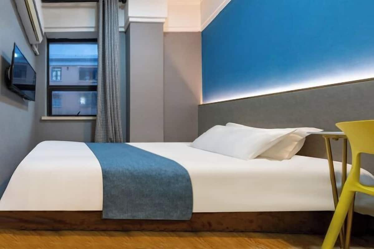 A hotel room with a bed, a TV mounted on the wall, a window with curtains, and a view of the outside.