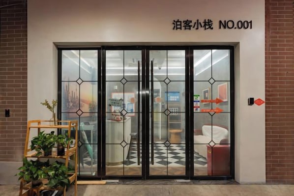 A hotel entrance with a glass door, a sign above the door, and a plant outside.