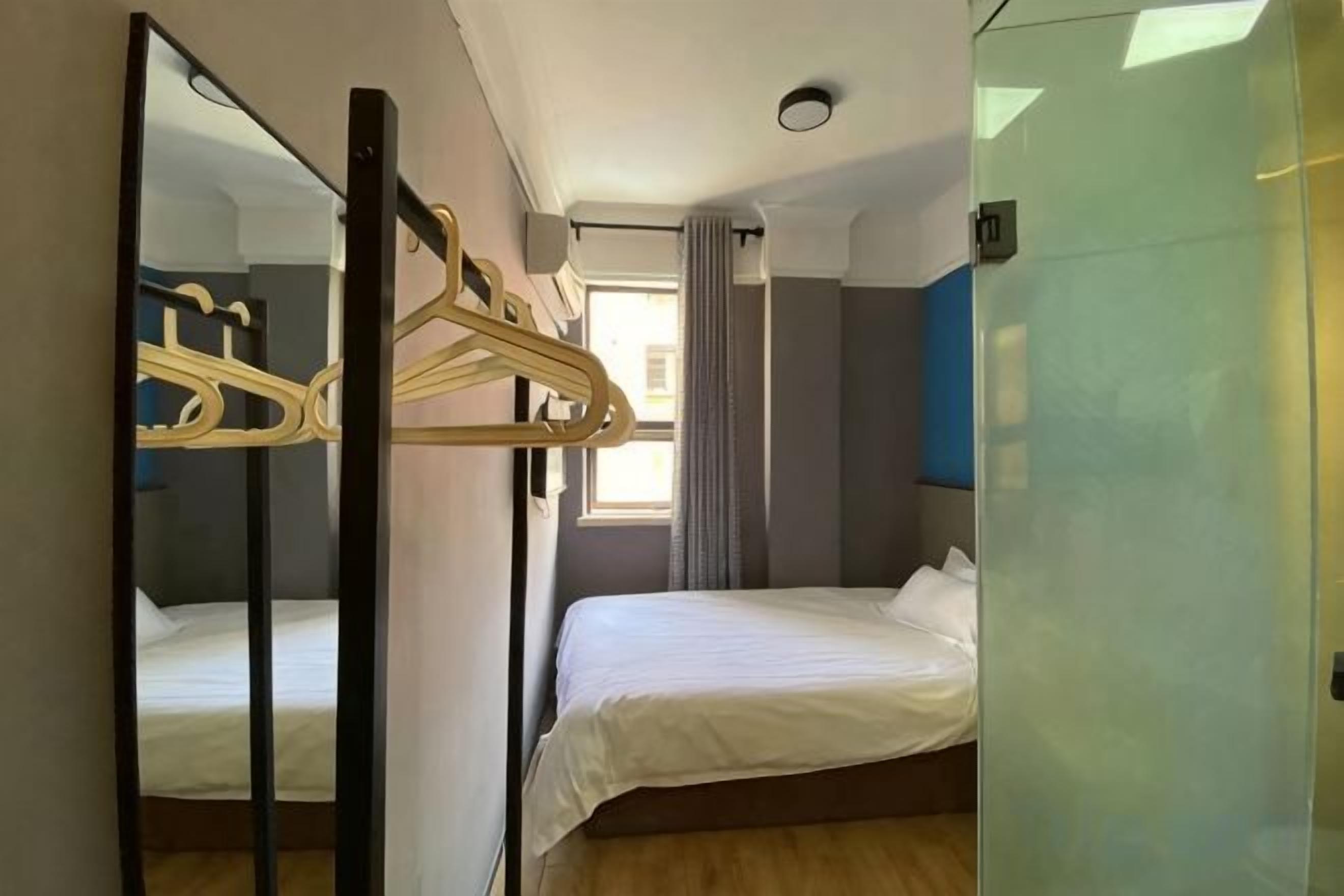 A bedroom with a bed, a mirror, a wardrobe, and a window with curtains.