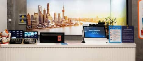 A reception desk with a large cityscape poster, a digital display, and informational signs.