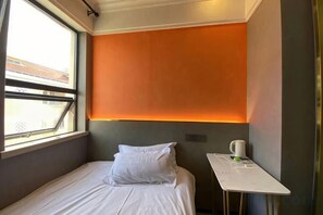 Un lit simple avec un oreiller blanc et une petite table sur laquelle se trouvent une tasse et un objet vert.