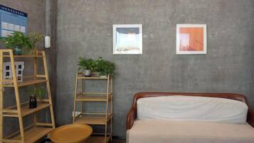Quarto com uma cama, duas prateleiras com plantas e duas fotografias emolduradas na parede.