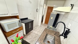 A compact kitchen with white cabinets, a microwave, a sink, and a small countertop.