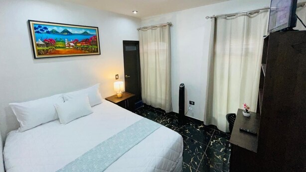 A hotel room with a bed, a desk, a TV, and a painting on the wall. - 3 bedroom in house in charming Panajachel with AC, WiFi. Enjoy your stay (panajachel)