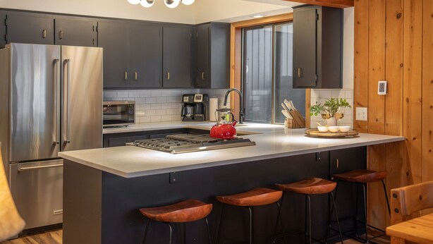 Een moderne keuken met donkere kasten, roestvrijstalen apparatuur, een centraal eiland met krukken en houten details.