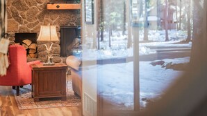 Een gezellige woonkamer met een stenen openhaard, een rode fauteuil en een houten bijzettafeltje met een lamp.