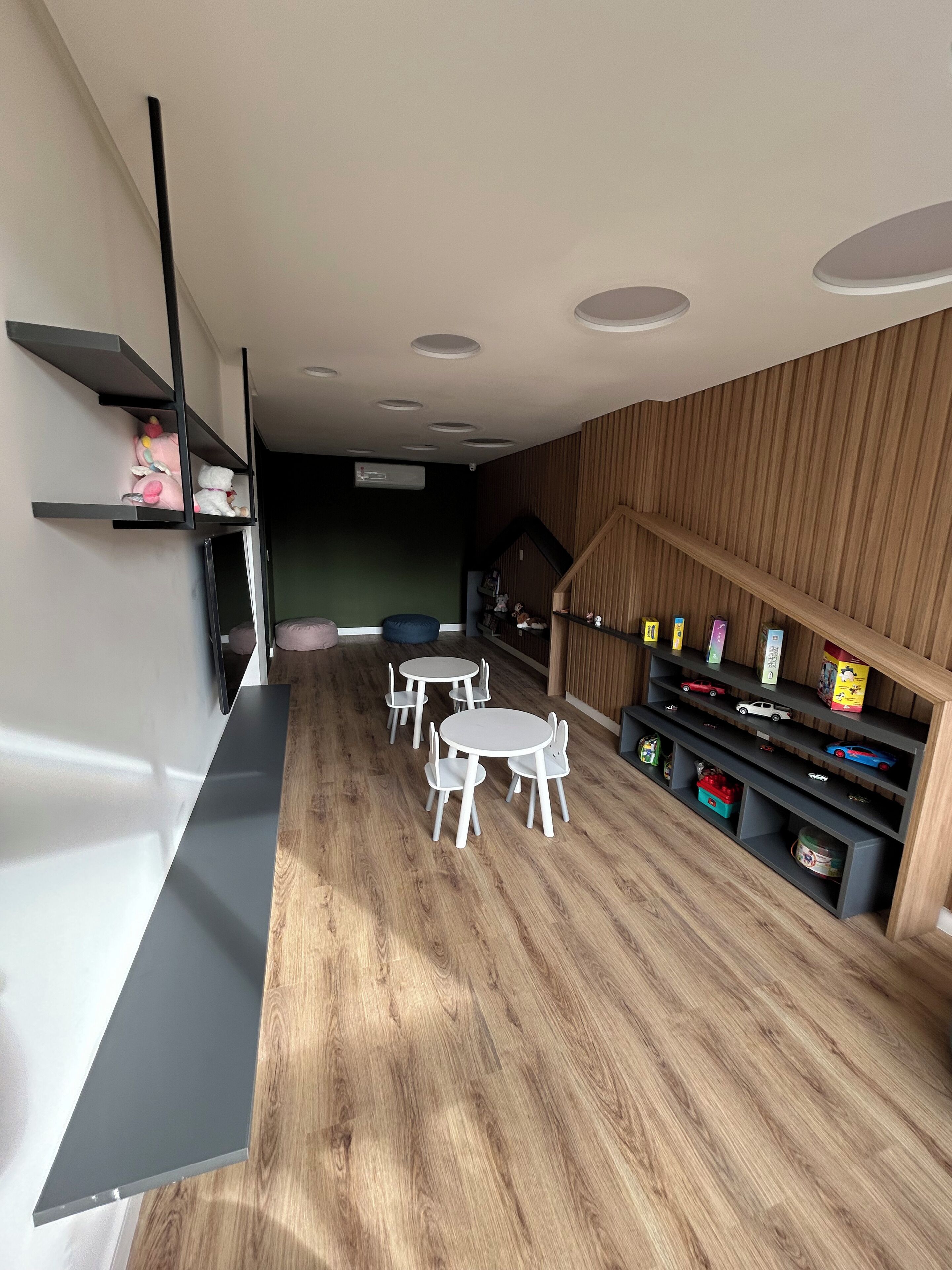 A modern interior with a dining area featuring white round tables and chairs, a wooden floor, and built-in shelves with toys and books.