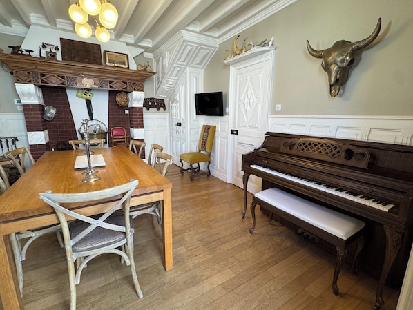 A dining area with a wooden table, chairs, a piano, and a bull skull decoration on the wall.