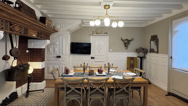 Une salle à manger avec une table en bois, quatre chaises, un lustre, un téléviseur et une décoration murale représentant un crâne de taureau.