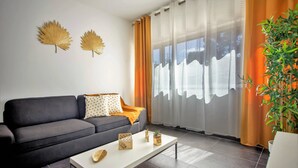 Un salon moderne avec un canapé gris foncé, une table basse blanche et des feuilles décoratives accrochées au mur.