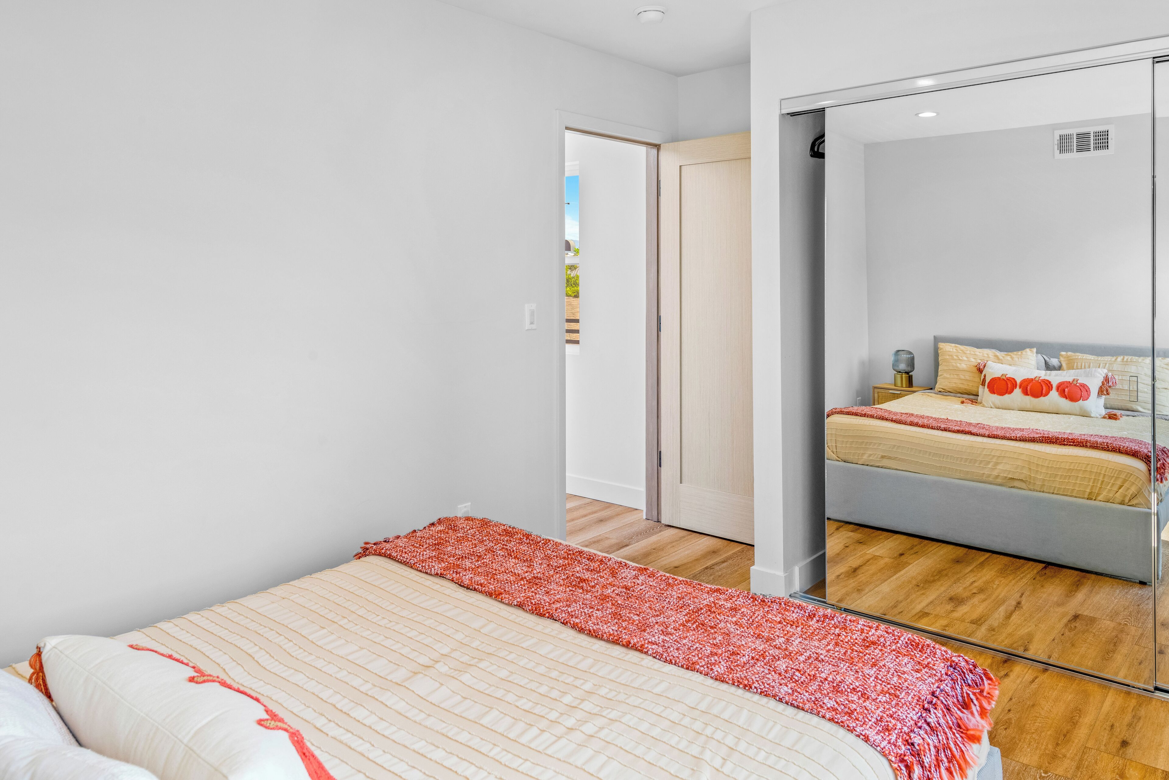 A modern bedroom with a bed, a mirror, and a door leading to another room.