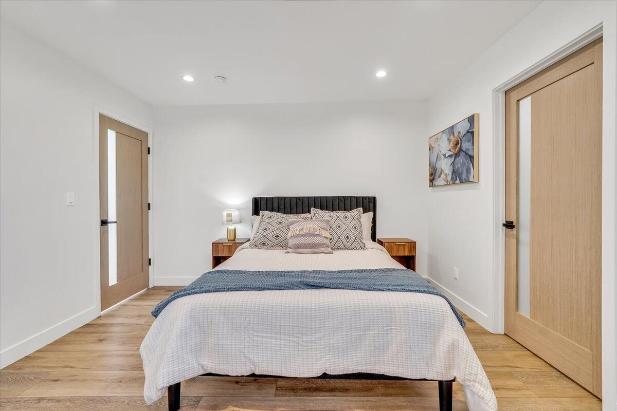 A bedroom with a bed, nightstands, a painting, and wooden doors.