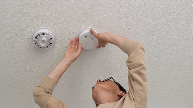 A person installing a smoke detector on a textured white wall. - Luxe Townhome | Newly-Built (Van Nuys)