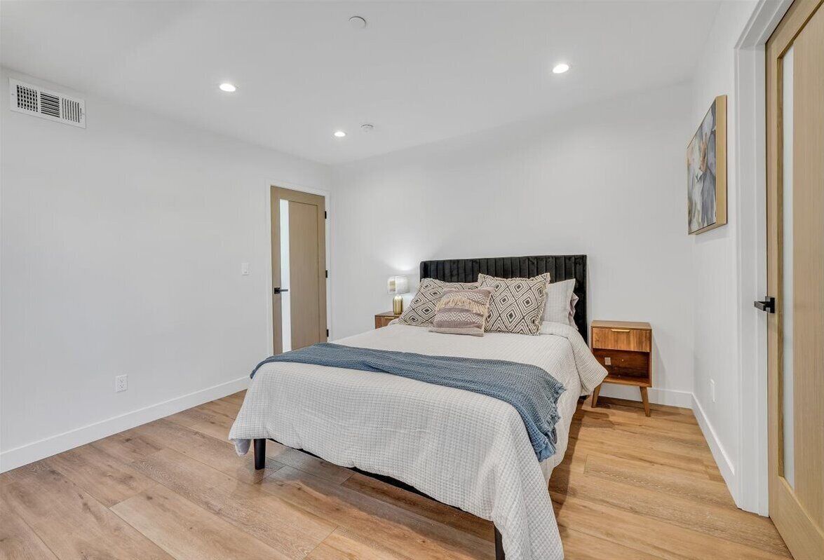 A bedroom with a bed, bedside tables, a nightstand, a door, and a ceiling vent.