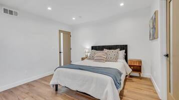 A bedroom with a bed, bedside tables, a nightstand, a door, and a ceiling vent.