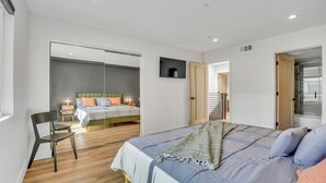 Een moderne slaapkamer met een groot bed, een stoel, een televisie en een schuifdeur naar een balkon.