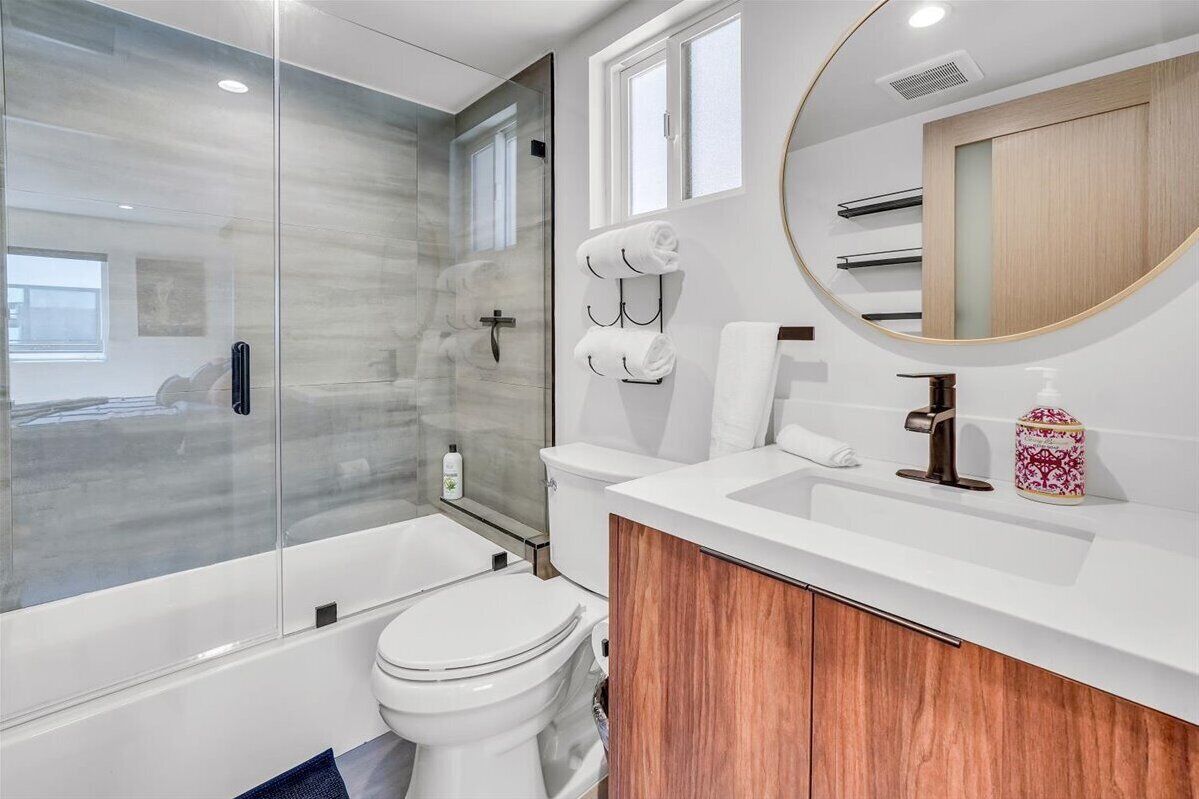 Une salle de bain moderne avec une douche à parois de verre, des toilettes blanches et un meuble-lavabo en bois avec un miroir.