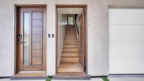 A modern building entrance with a wooden door, a staircase leading to a garage, and a white garage door. - Luxe Townhome | Newly-Built (Van Nuys)