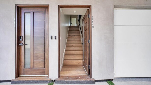 Een moderne gevel met een houten deur, een trap naar een garage, en een witte garagepoort.