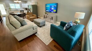 Un salon comprenant un canapé, un pouf et un fauteuil turquoise. Un téléviseur à écran plat est fixé au mur.