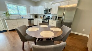 Une cuisine moderne avec des meubles blancs, un réfrigérateur en acier inoxydable et une table de salle à manger ronde, accompagnée de quatre chaises.