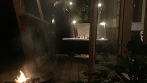 Een terras in gedempt licht met een vuurkorf, een badkuip en enkele planten.