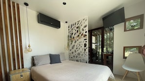 Een slaapkamer met een bed, een koffer, een wandairconditioner, een decoratief paneel en uitzicht op de omgeving.