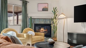 A living room with a fireplace, two armchairs, a coffee table, and a television.
