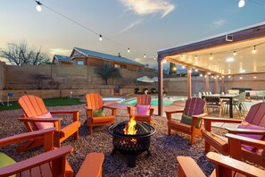 Ein Terrassenbereich im Freien mit Adirondack-Stühlen, einer Feuerstelle und einem Pool.