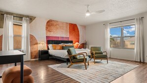 A modern bedroom with a bed, two chairs, a desk, and a large window.
