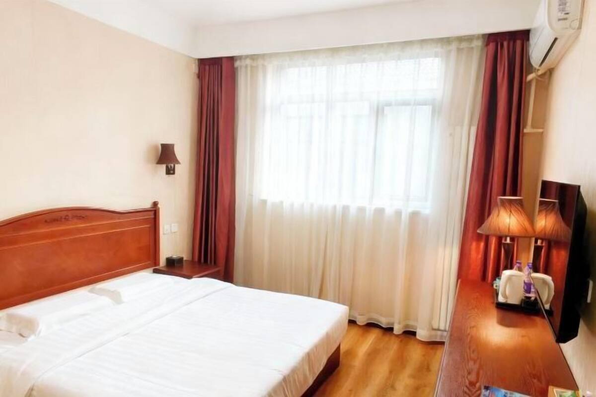 A hotel room with a bed, a nightstand, a lamp, a TV, and a window with curtains.