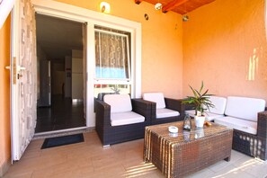 A balcony with wicker furniture, a potted plant, and a glass coffee table.