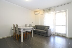 A dining area with a table and chairs, a sofa, and a sliding glass door.