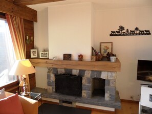 A cozy living room with a stone fireplace, wooden mantel, and various decorative items.