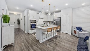 A modern kitchen with white cabinetry, a central island with bar stools, stainless steel appliances, and pendant lighting. - The Par-fect Stay at Barefoot Resort (North Myrtle Beach)