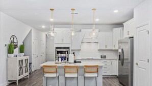 A modern kitchen with white cabinetry, a stainless steel refrigerator, and a central island with bar stools. - The Par-fect Stay at Barefoot Resort (North Myrtle Beach)