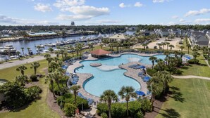 A large, irregularly shaped pool with multiple sections and a surrounding deck with lounge chairs and umbrellas. - The Par-fect Stay at Barefoot Resort (North Myrtle Beach)