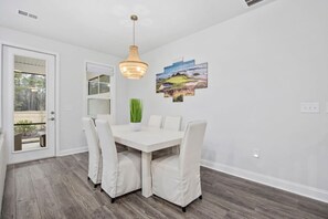 Un coin repas avec une table blanche, quatre chaises, un luminaire suspendu et une fenêtre donnant sur un paysage.