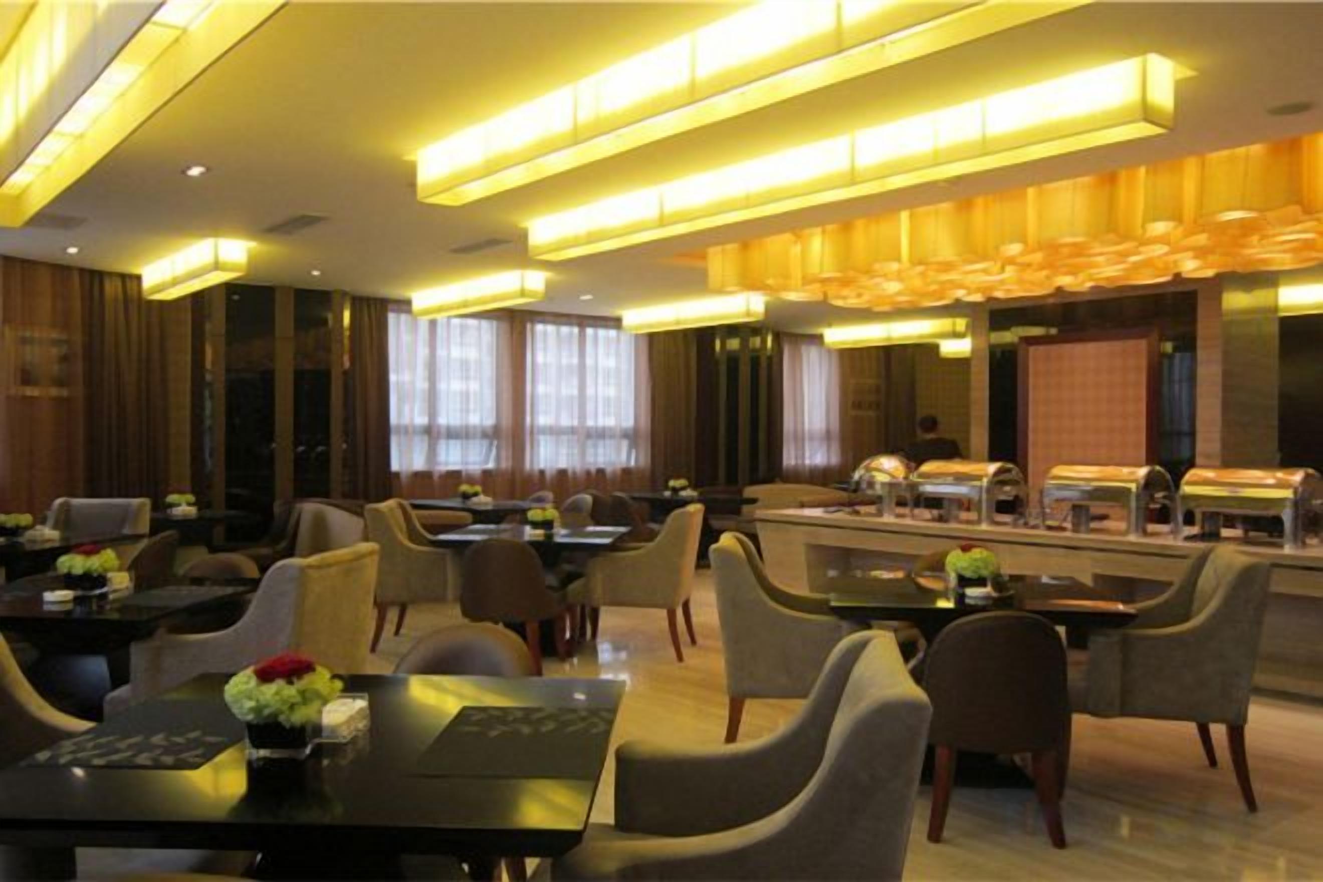 Espaço de refeições moderno em hotel, com mesas, cadeiras e serviço de buffet.
