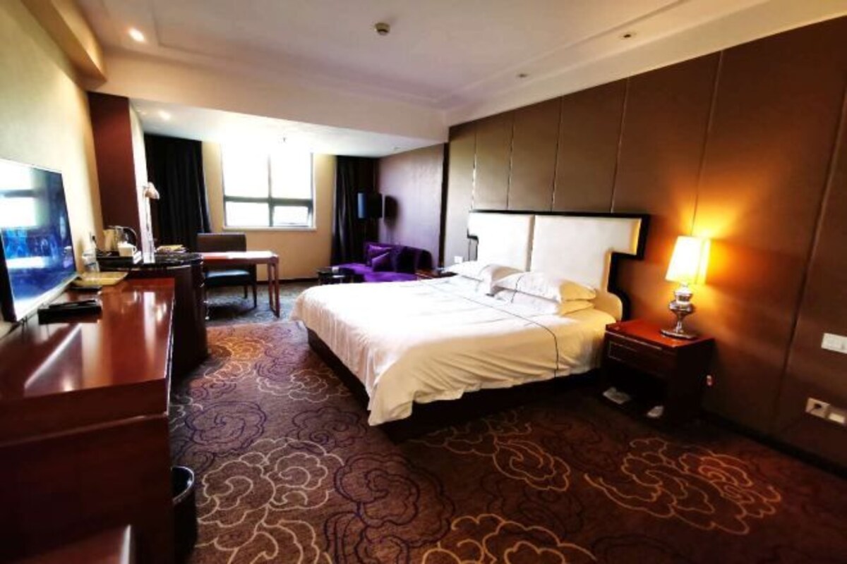 A hotel room with a bed, a desk, a chair, a TV, and a lamp.