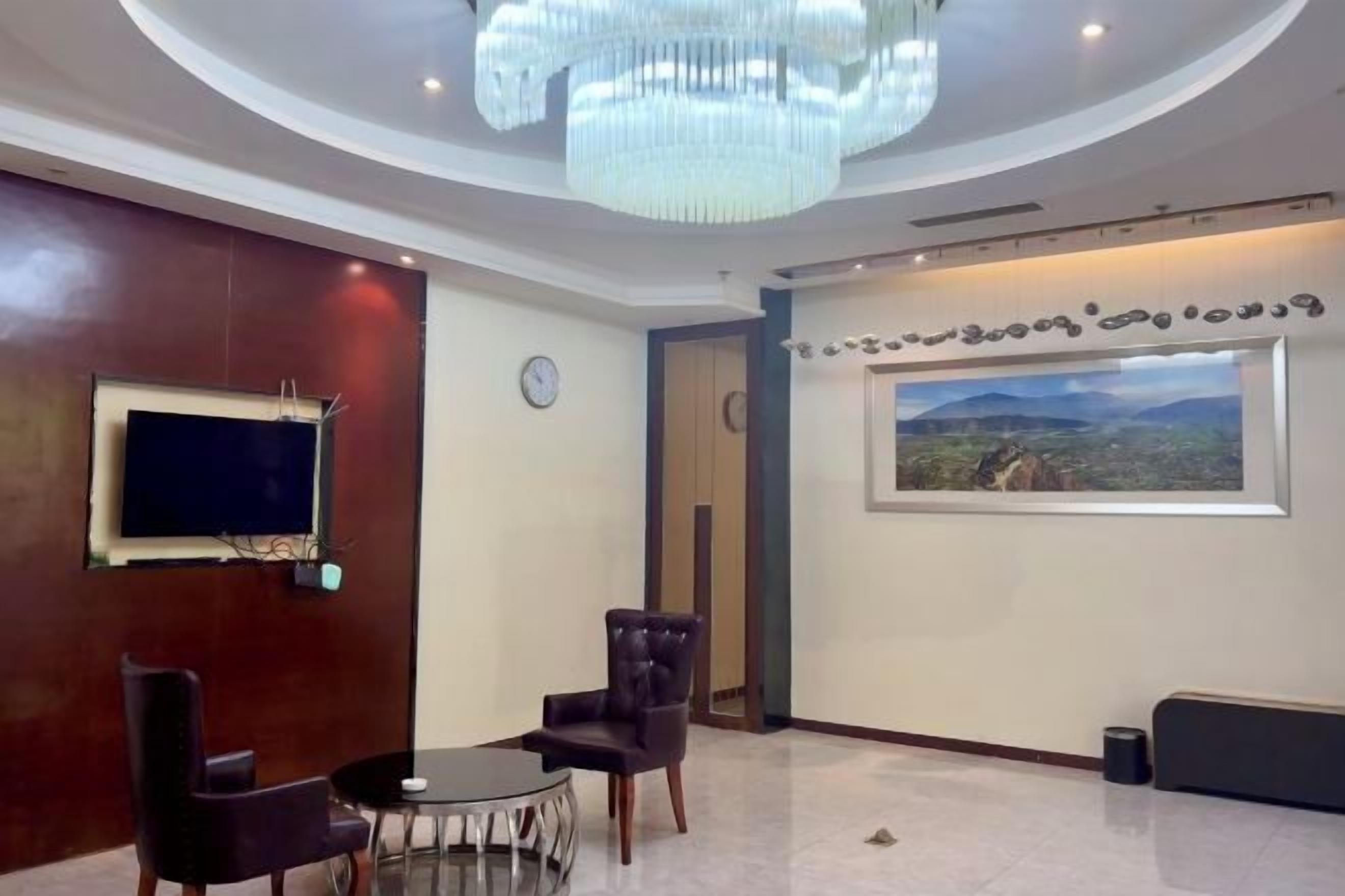 A lobby with a chandelier, a TV mounted on a wooden wall, a round table with chairs, and a large window with a mountain view.