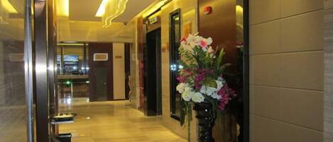 A hotel hallway with a vase of flowers, a reception desk, and a door.