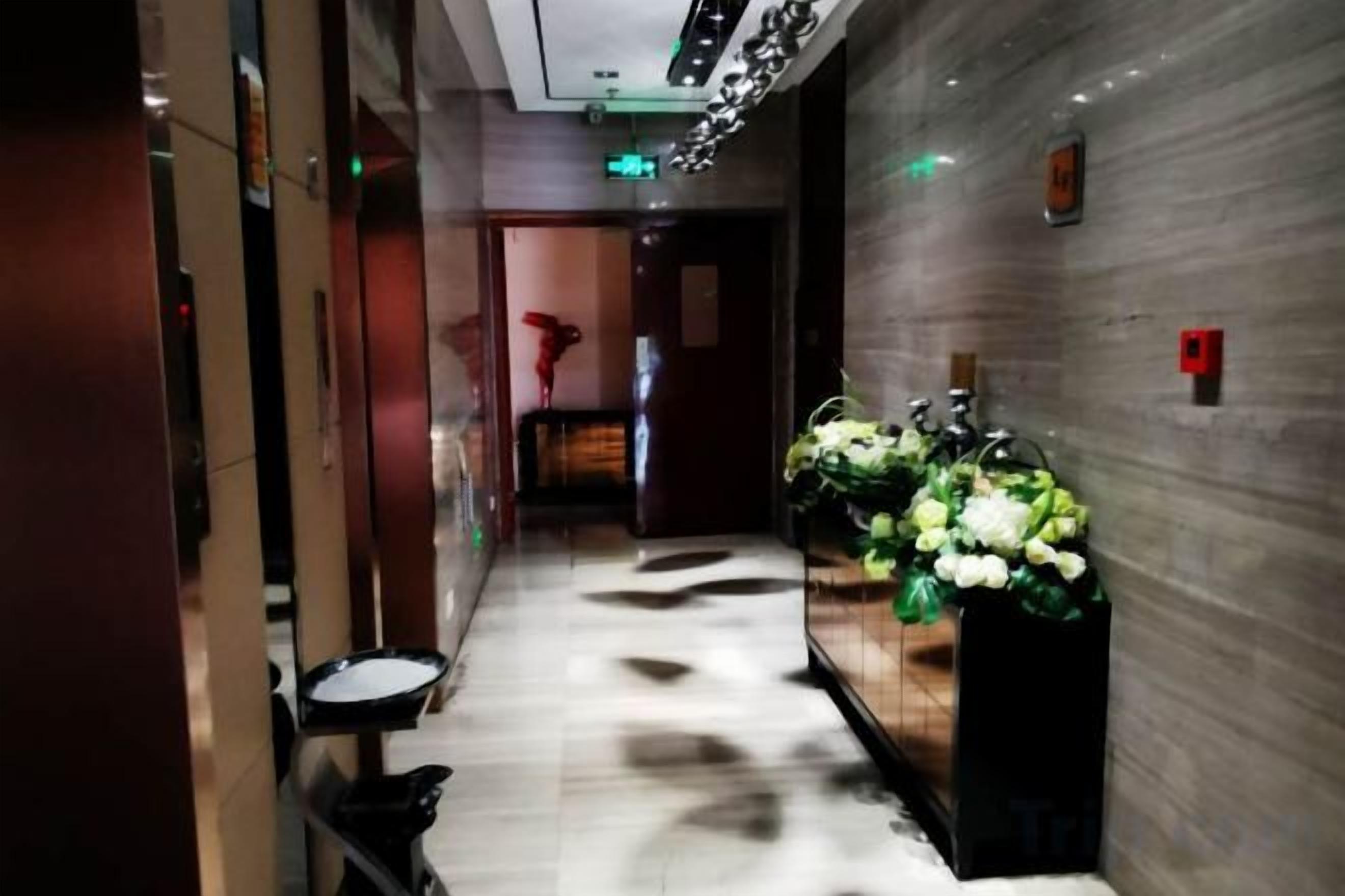 A hotel corridor with a marble floor, a reception desk, and a wall-mounted fire alarm.
