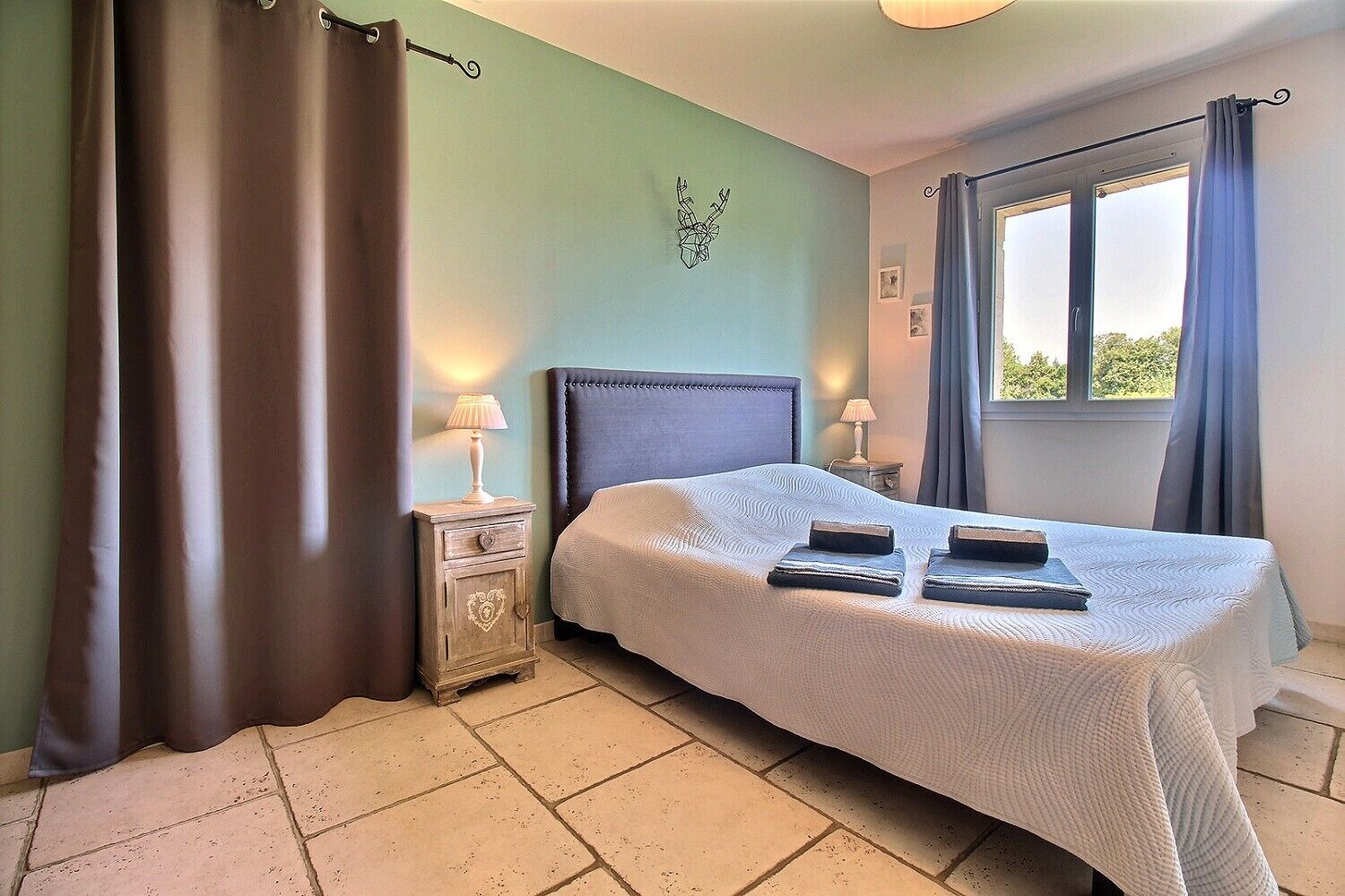 A bedroom with a bed, nightstands, a window with curtains, and a wall decoration.