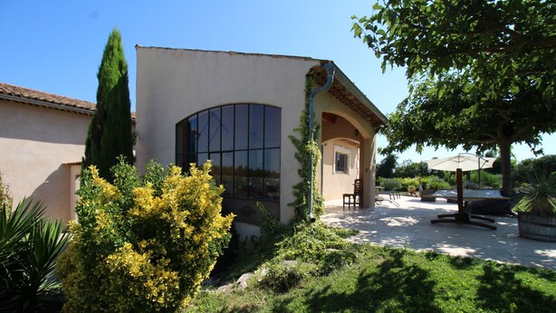 A building with a large arched window, a patio area with outdoor furniture, and a well-maintained garden with various plants. - The Malirel Estate (Cavaillon)